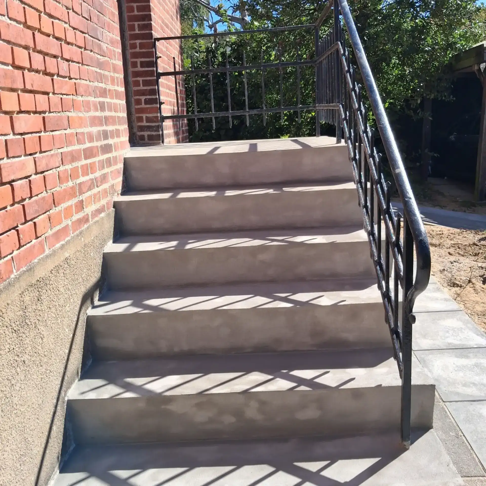 Udendørs trappe med betontrin og sort metal gelænder.